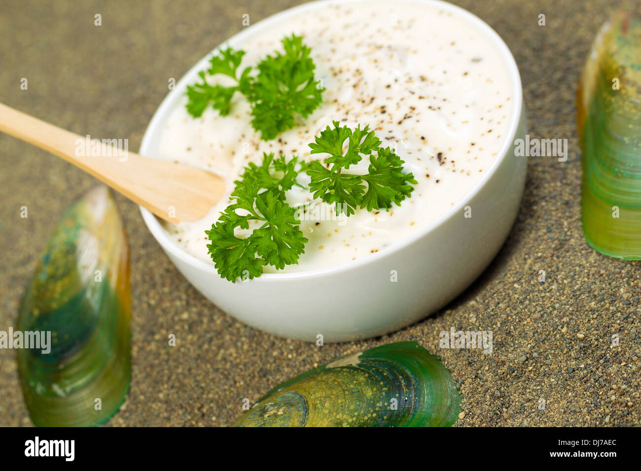 frische Muschelsuppe im weißen Tasse sowie Petersilie und Holzlöffel innen mit Sand und Ruhe Muscheln umgebenden Schale Stockfoto