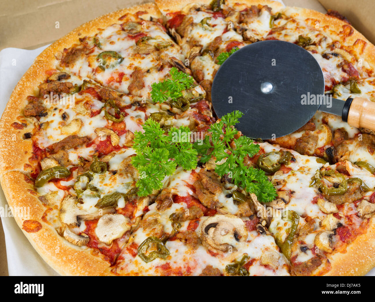 Foto von frischer Pizza mit Petersilie, Champignons und Paprika in einer Box mit Cutter an der Spitze Stockfoto