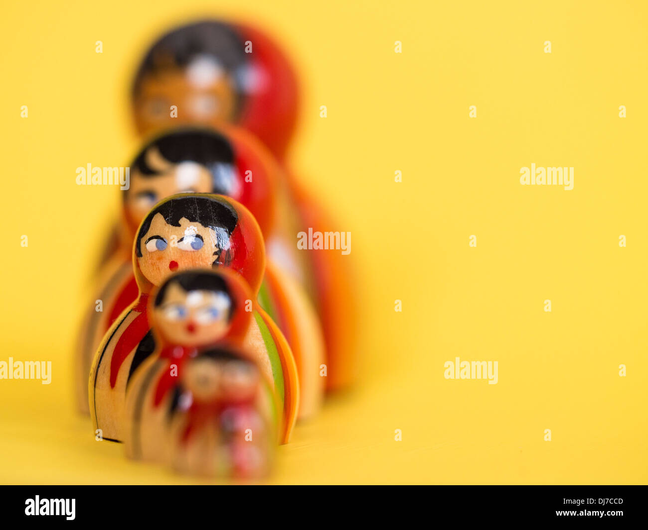 Gruppe von russischen Matroschka Puppen in einer Reihe mit selektiven Fokus auf eine Puppe, umrahmt von einem hellgelben Hintergrund. Stockfoto