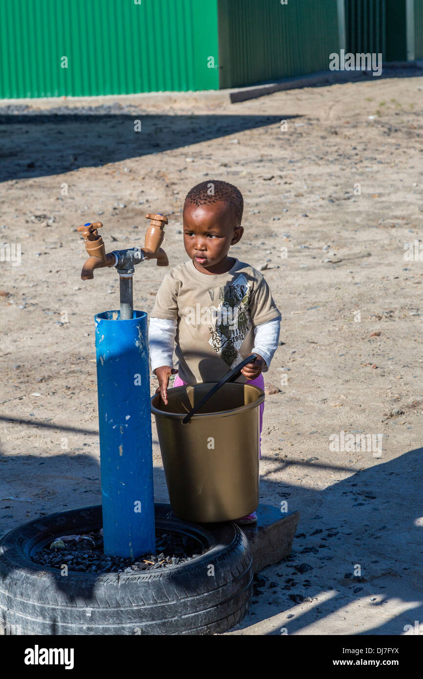 Südafrika, Cape Town, Khayelitsha Township. Kleiner Junge mit Eimer Gemeinschaft Wasserhahn zu studieren. Stockfoto