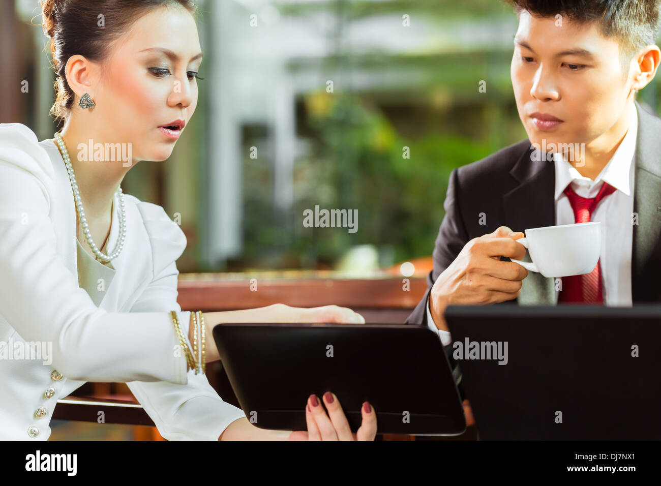 Zwei asiatische chinesische Büro Personen oder Geschäftsmann und Geschäftsfrau, die mit einem Business-Meeting in einer Hotellobby Dokumente diskutieren Stockfoto