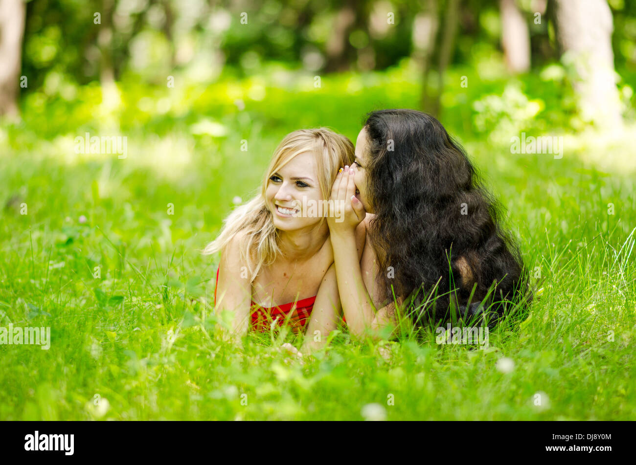 zwei flüsternde Freundinnen liegen auf dem Rasen Stockfoto