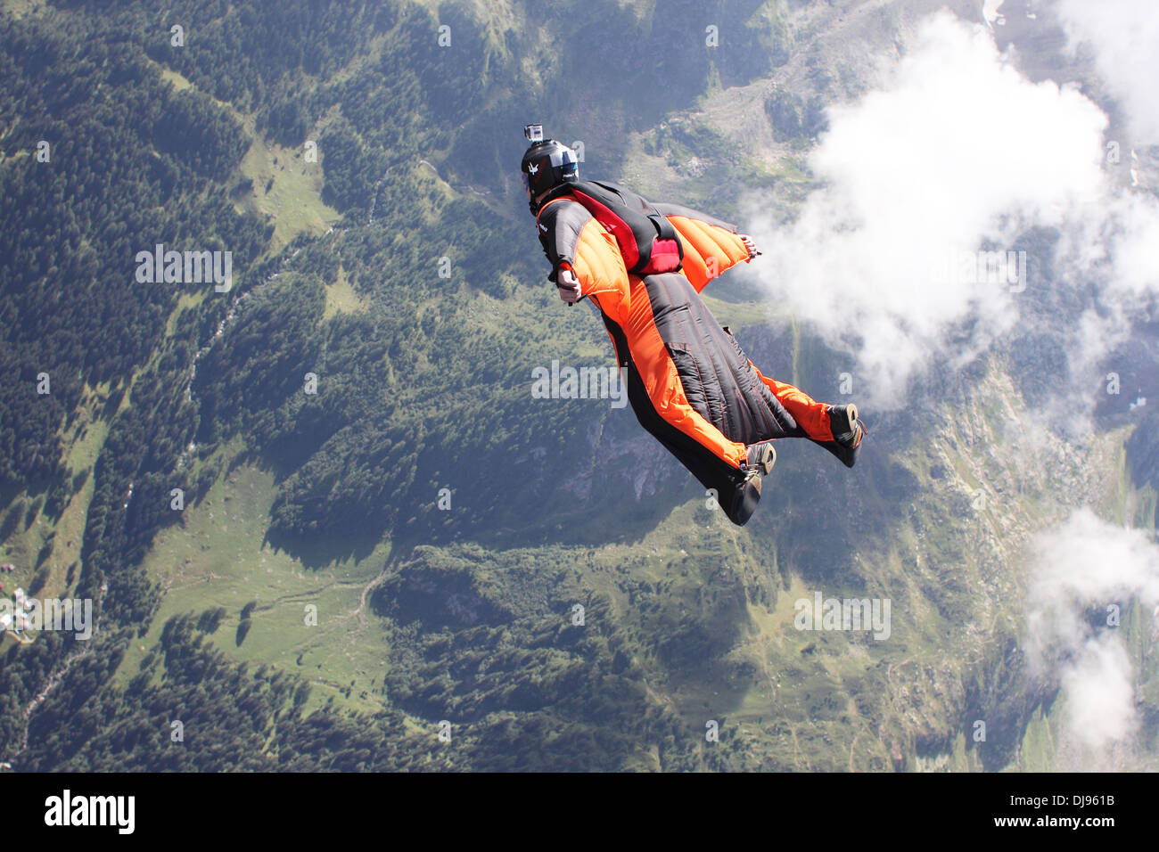 Mann im Overall mit orange Wings fliegt über Berge neben Wolken. Er ist sehr glücklich, in den Himmel steigen. Stockfoto