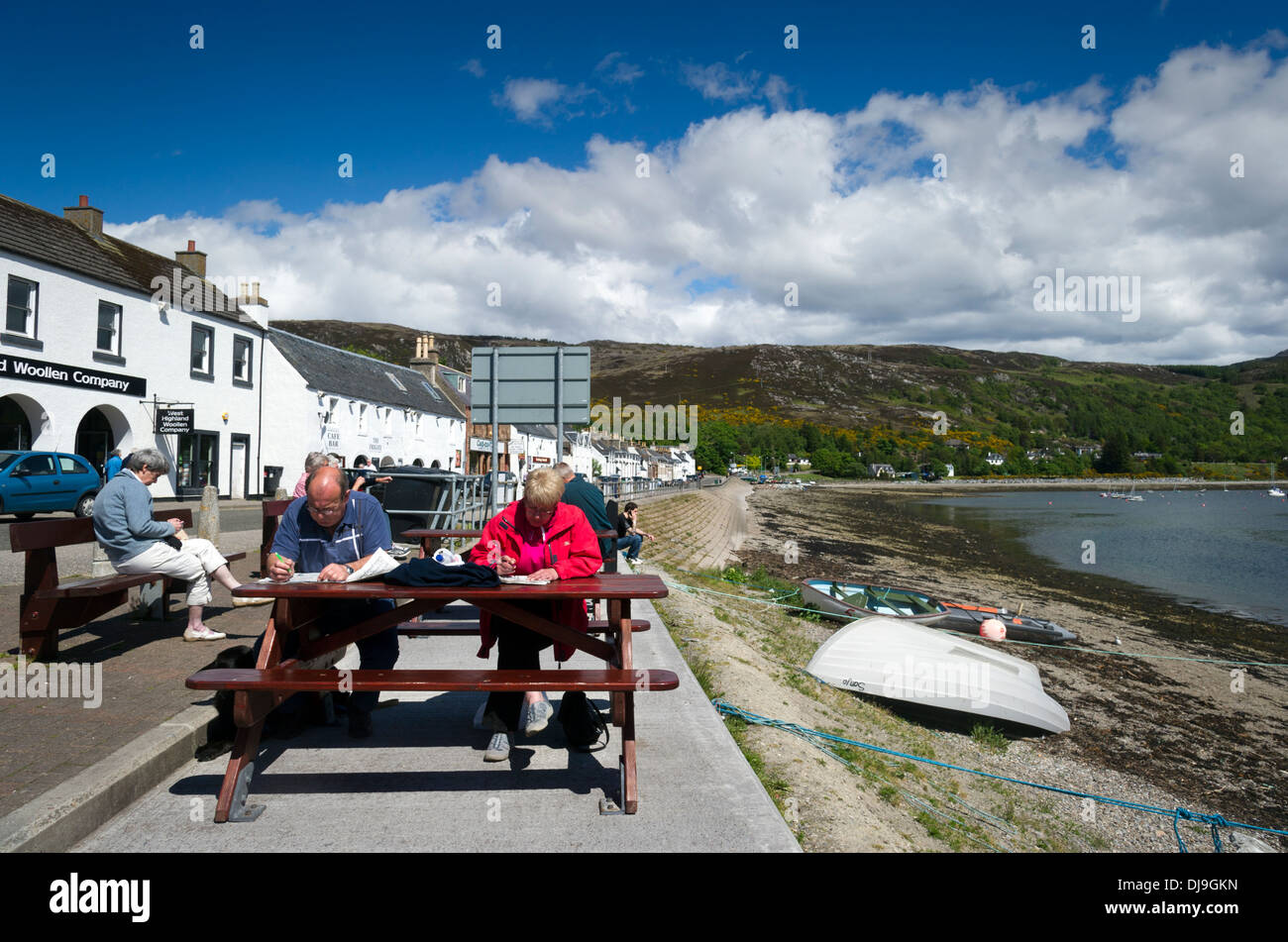 Leute sitzen, entspannen und lesen außerhalb an einem sonnigen Tag Ullapool, Ross & Cromarty, West Schottland UK Stockfoto