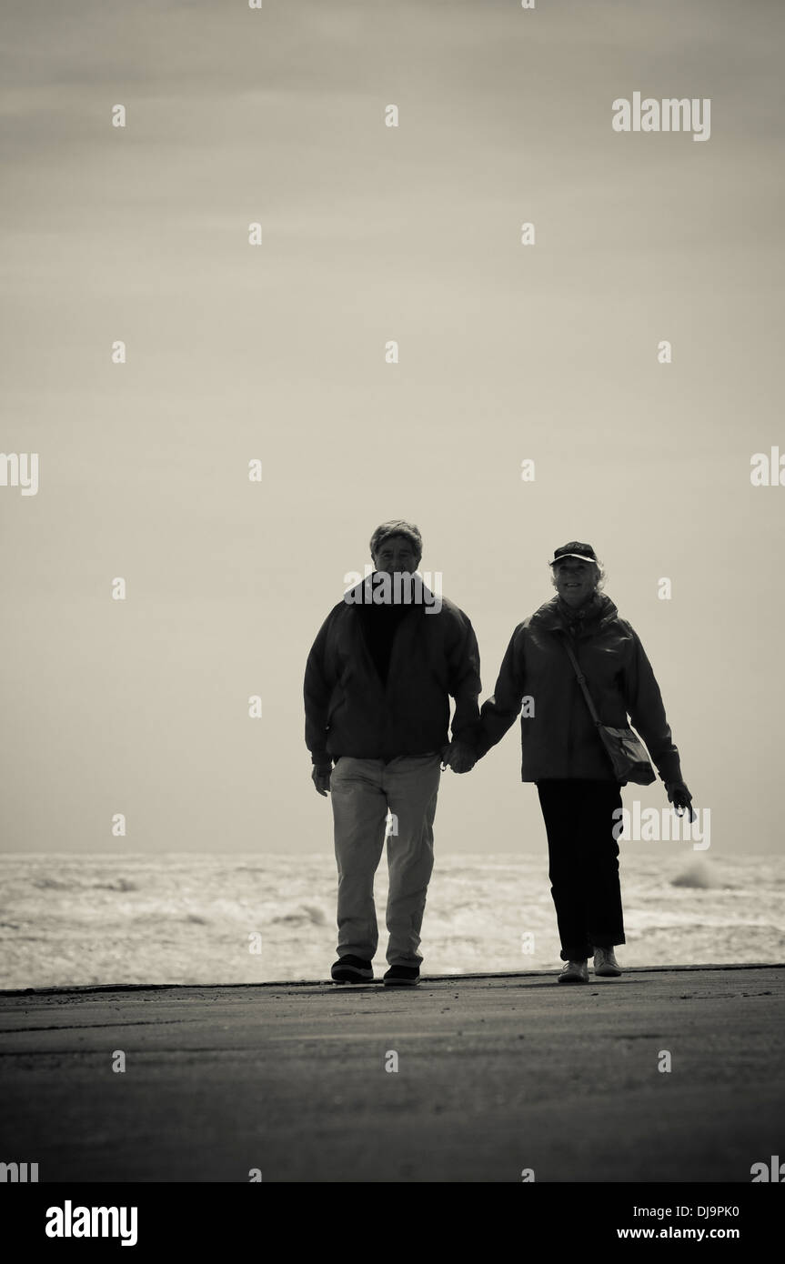 Ein paar ältere Menschen gehen Hand in Hand am Strand. Stockfoto
