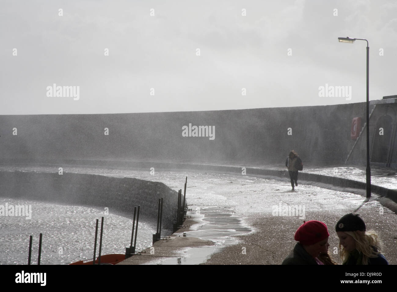 Person, die durch Gischt Absturz über Ufermauer im Sturm Stockfoto