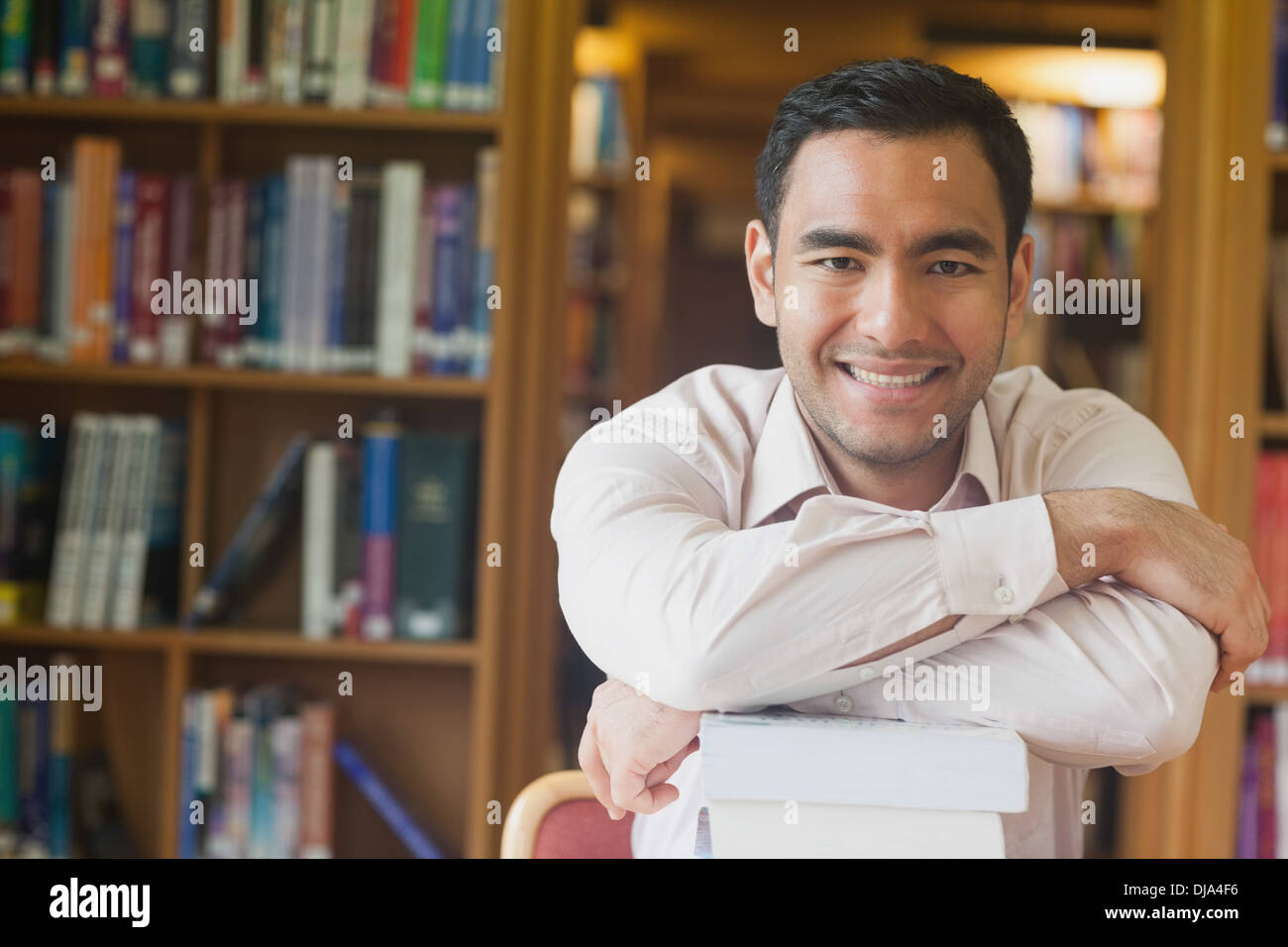 Fröhliche attraktive Mann posiert stützte sich auf einen Stapel Bücher in der Bibliothek Stockfoto
