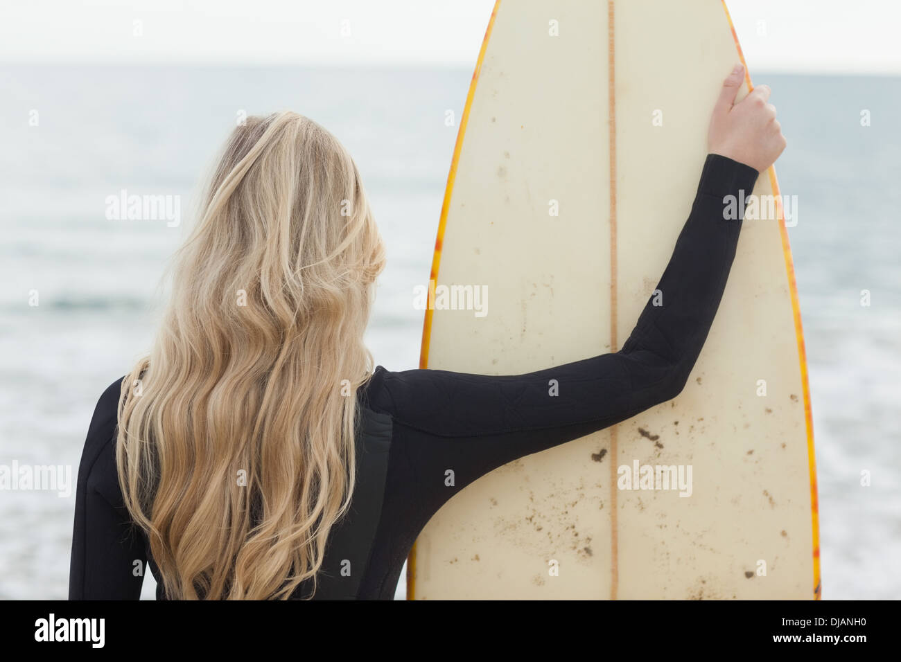 Rückansicht von einer Blondine im Neoprenanzug mit Surfbrett am Strand Stockfoto