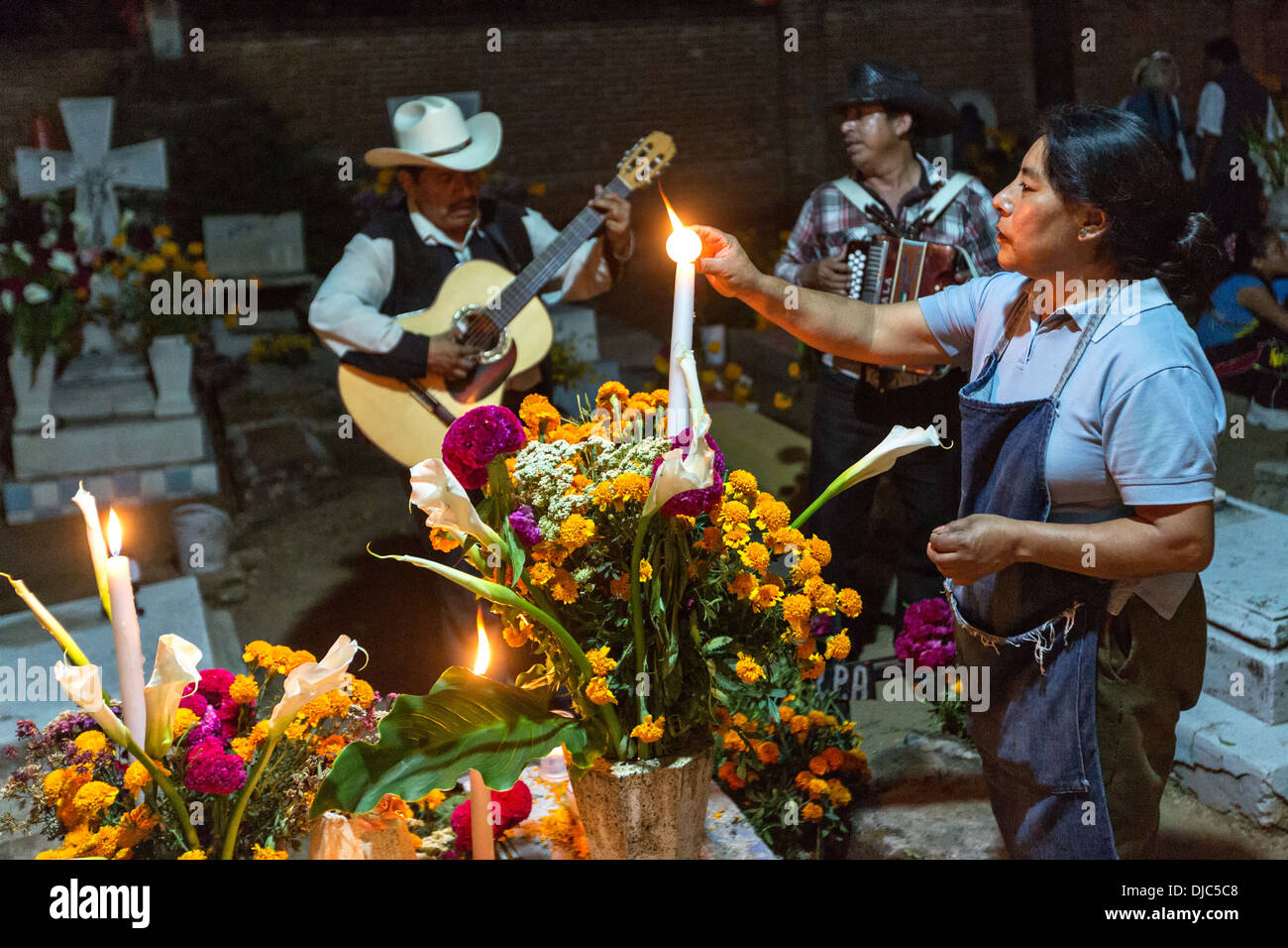 Eine Mexikanerin leuchtet eine Kerze am Grab von Verwandten als eine Mariachi-Band für tot Festivaltag spielt. Stockfoto