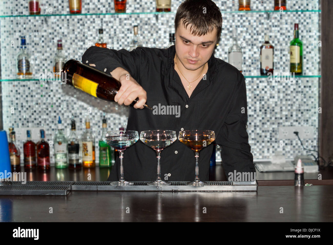 Barkeeper, die Getränke in einer Bar in drei eleganten cocktail-Gläser gießen, als er eine exotische Mischung bereitet Stockfoto