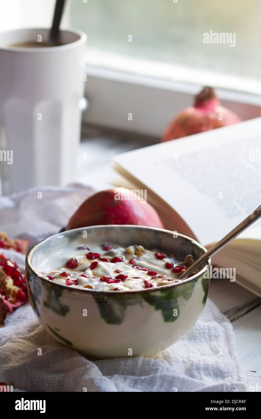 Gesundes Frühstück mit Granatapfel in Joghurt, Kaffee und aufgeschlagenes Buch Stockfoto