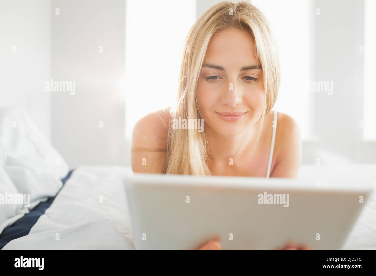 Fröhliche Blondine mit digital-Tablette auf ihrem Bett Stockfoto