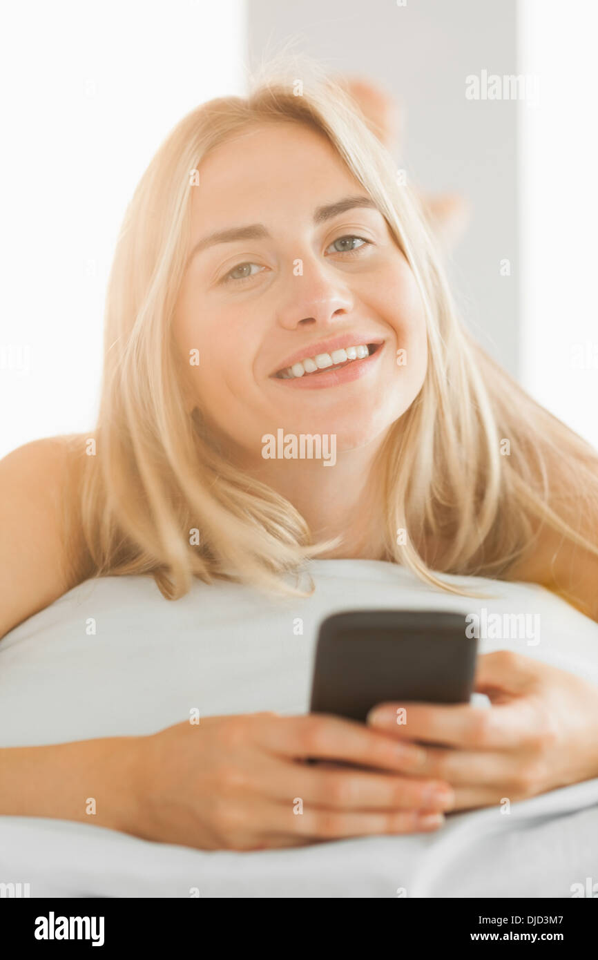 Fröhliche Blondine liegen auf ihrem Kissen, eine SMS senden Stockfoto