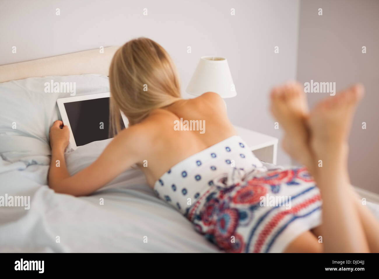 Frau trägt Kleid auf Bett liegend mit ihrem TabletPC Stockfoto