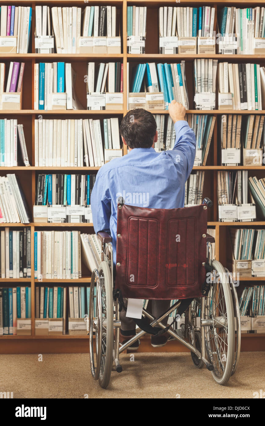 Mann im Rollstuhl setzen wieder ein Buch im Bücherregal Stockfoto