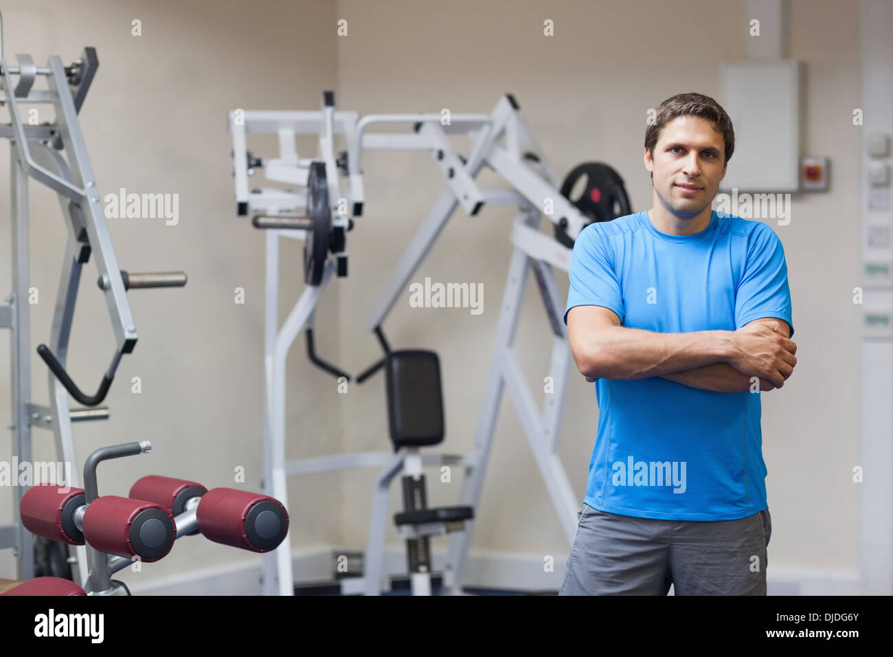 Lächelnde Trainer mit Arme gekreuzt gegen Lat Maschine im Fitness-Studio Stockfoto