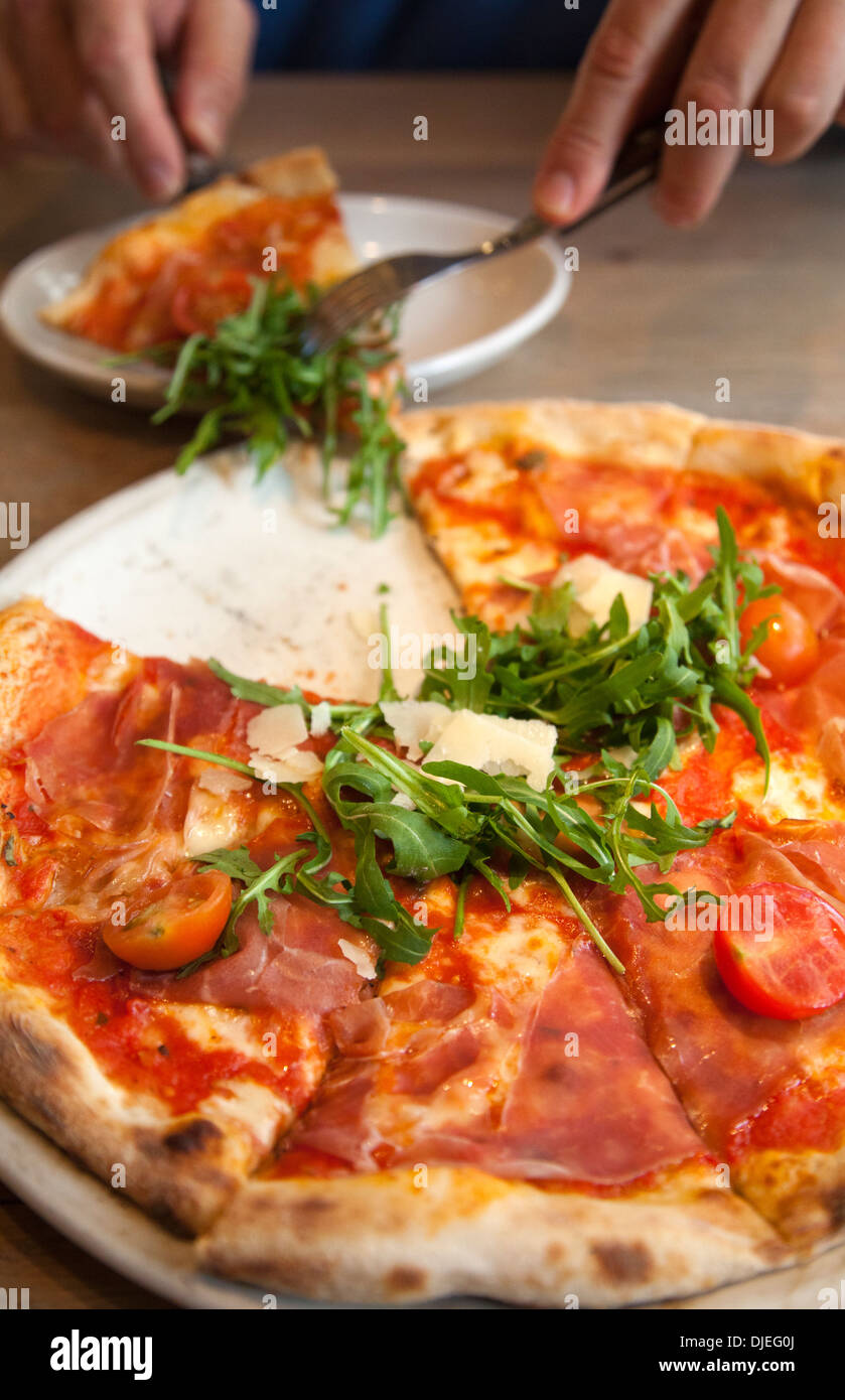 Mann unter Stück San Daniele Pizza mit Rucola und Prosciutto Stockfoto