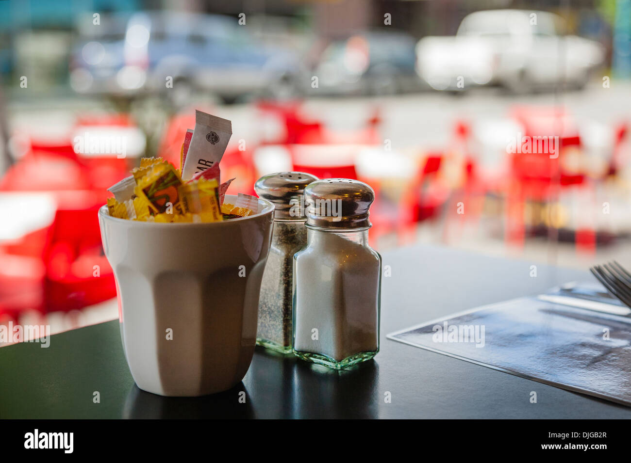 Blick aus einem Café-Fenster auf die Straße und Tische und Stühle draußen. Salzen, pfeffern und Pakete von Zucker auf den Tisch. Stockfoto