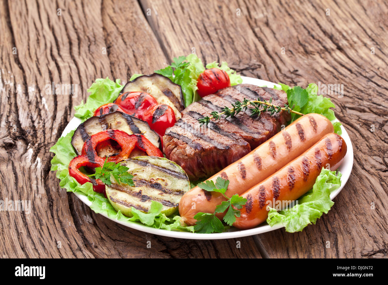 Gegrilltes Steak, Wurst und Gemüse über Salat Blätter auf einem Holztisch. Stockfoto