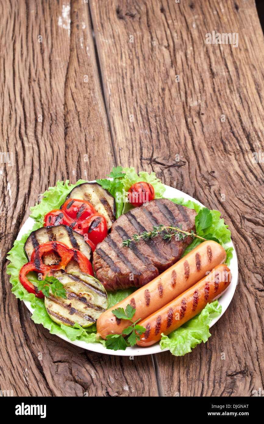 Gegrilltes Steak, Wurst und Gemüse über Salat Blätter auf einem Holztisch. Stockfoto