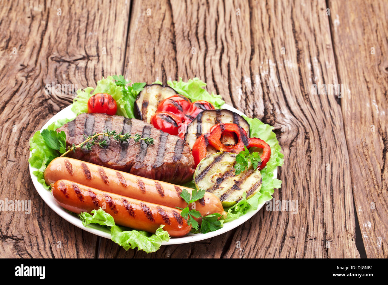 Gegrilltes Steak, Wurst und Gemüse über Salat Blätter auf einem Holztisch. Stockfoto