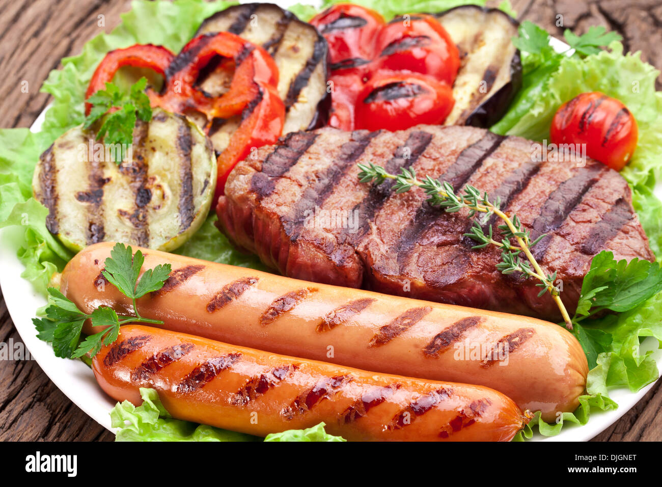 Gegrilltes Steak, Wurst und Gemüse über Salat Blätter auf einem Holztisch. Stockfoto