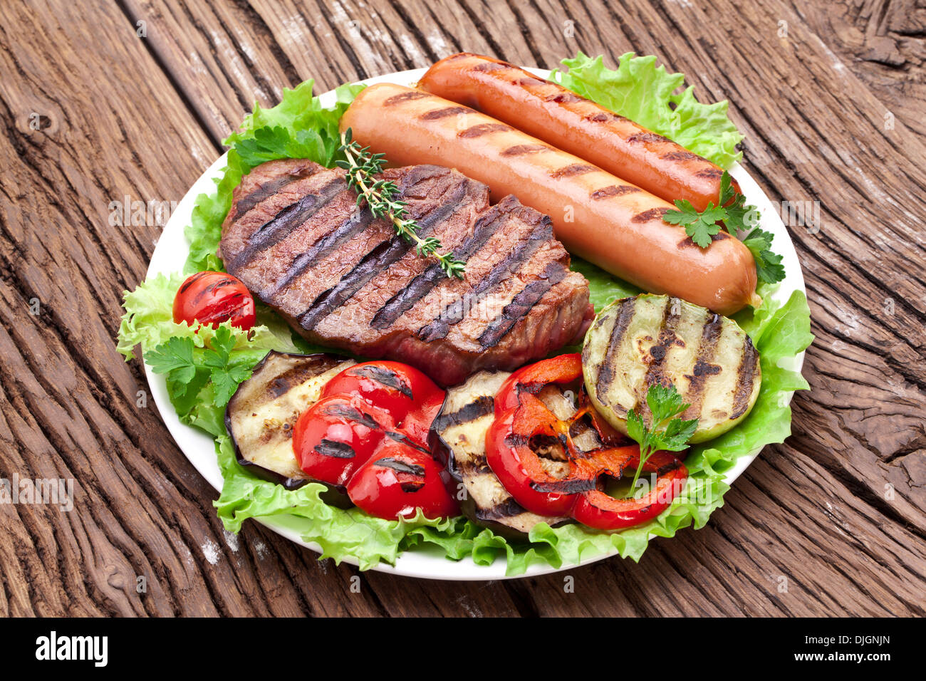 Gegrilltes Steak, Wurst und Gemüse über Salat Blätter auf einem Holztisch. Stockfoto