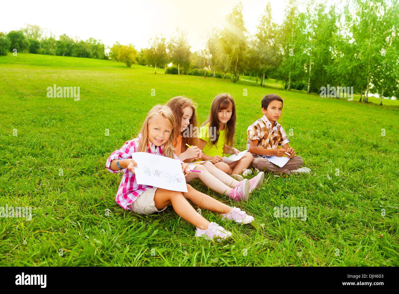 Vier kleine 6 und 7 Jahre alt Kinder sitzen auf der Wiese und zeichnen von Bildern Stockfoto