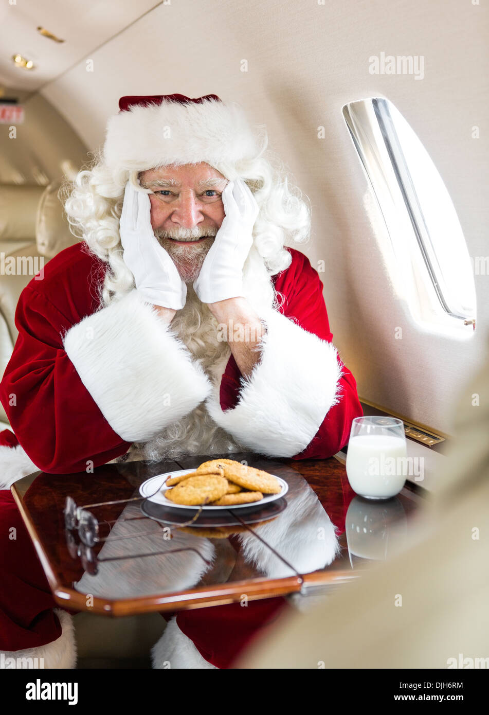 Weihnachtsmann mit Cookies und Milch sitzen im Privatjet Stockfoto