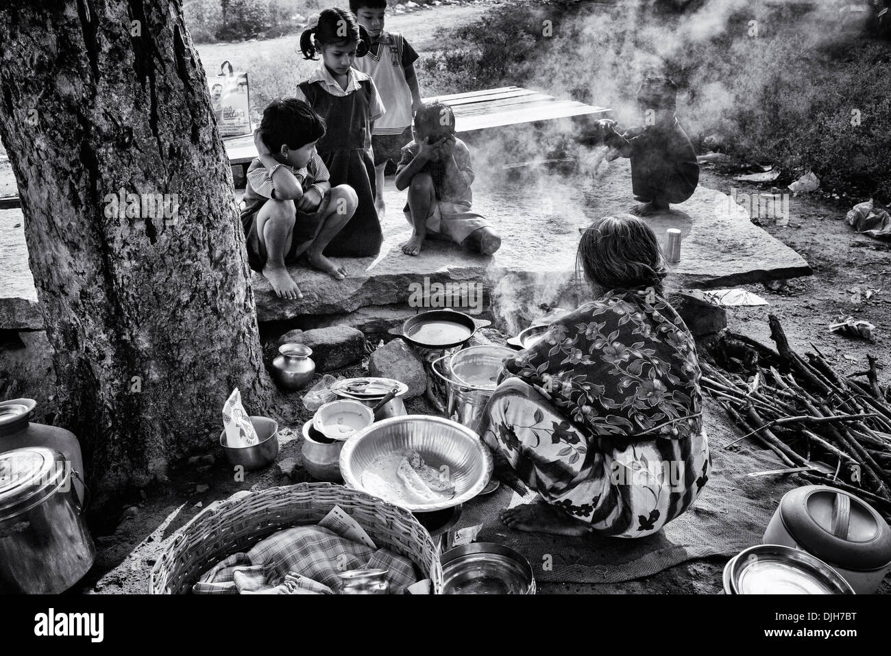 Indische Frau Kochen Dosa für Kinder im ländlichen Indien Dorfstraße. Andhra Pradesh, Indien. Schwarz und weiß. Stockfoto