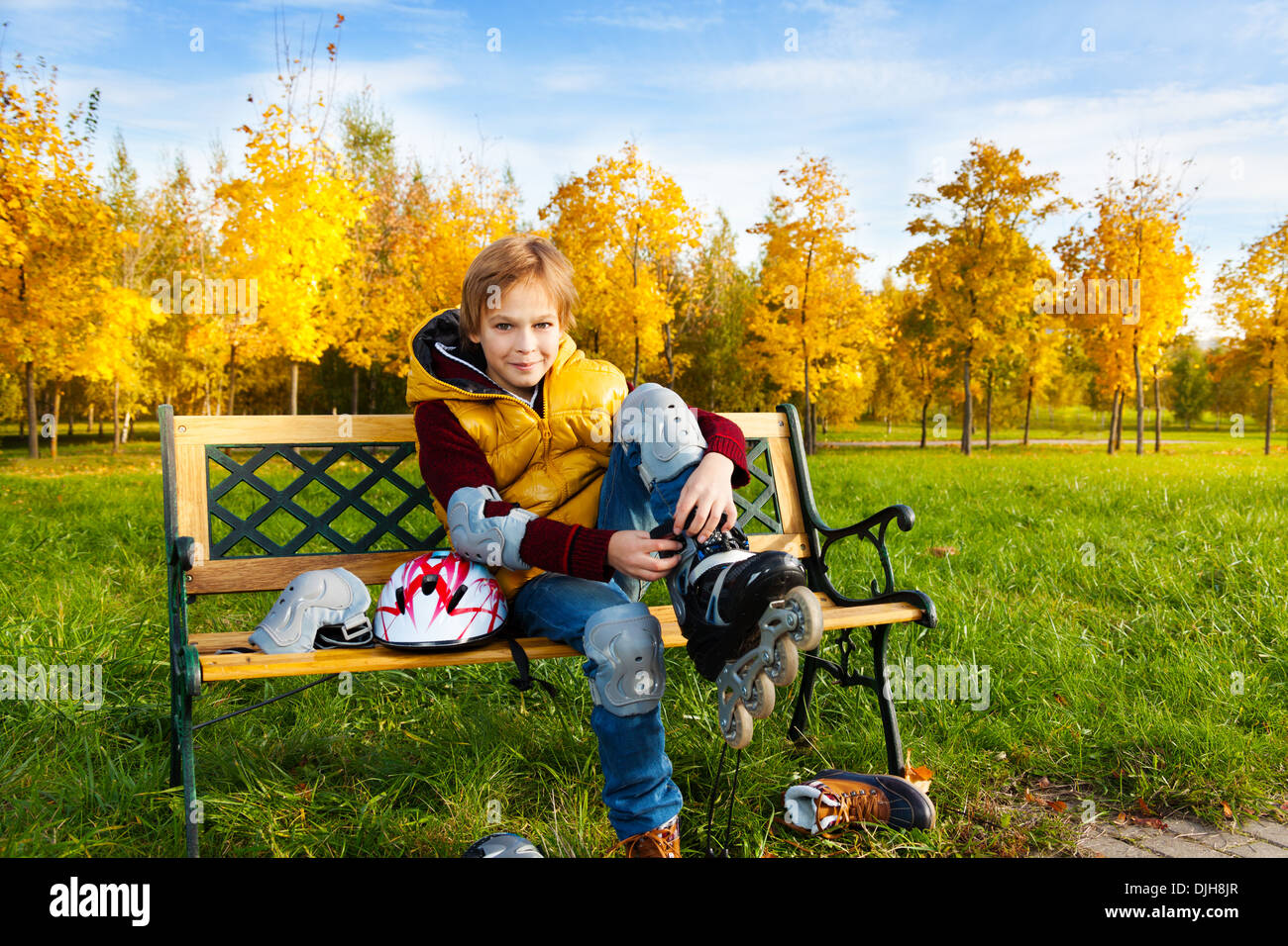 10 Jahre alter Junge setzen auf Inlineskates auf der Bank sitzen, an sonnigen Herbsttag Eislaufen Stockfoto
