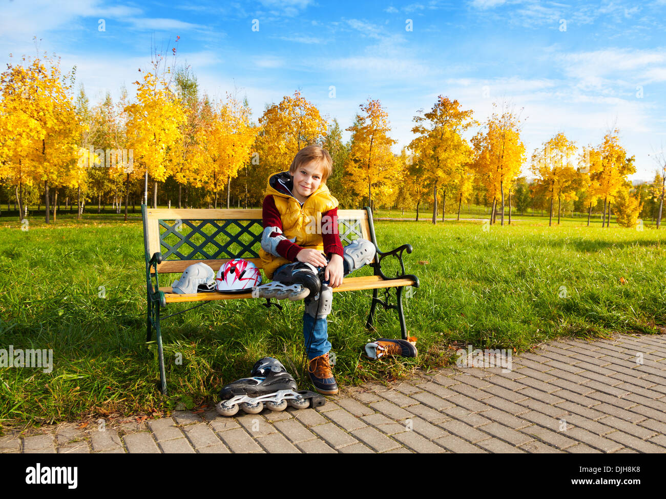 Nette junge im Herbst Freizeitkleidung setzen auf Rollschuhen sitzen auf der Bank im park Stockfoto