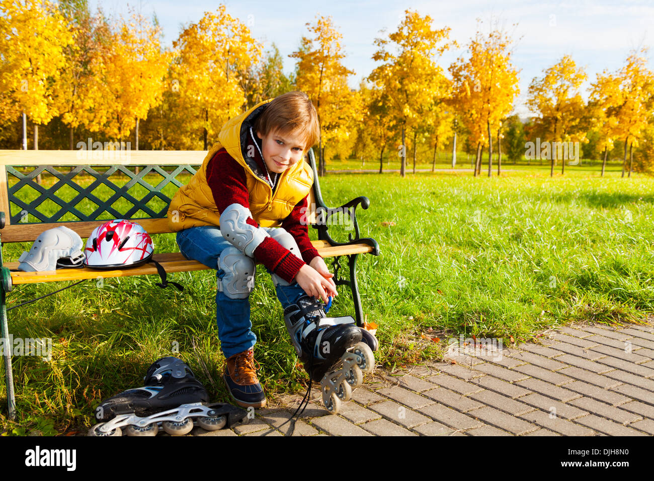 Schöne 10 Jahre alten Buben im Herbst Freizeitkleidung setzen auf Rollschuhen auf der Bank im Park sitzen Stockfoto