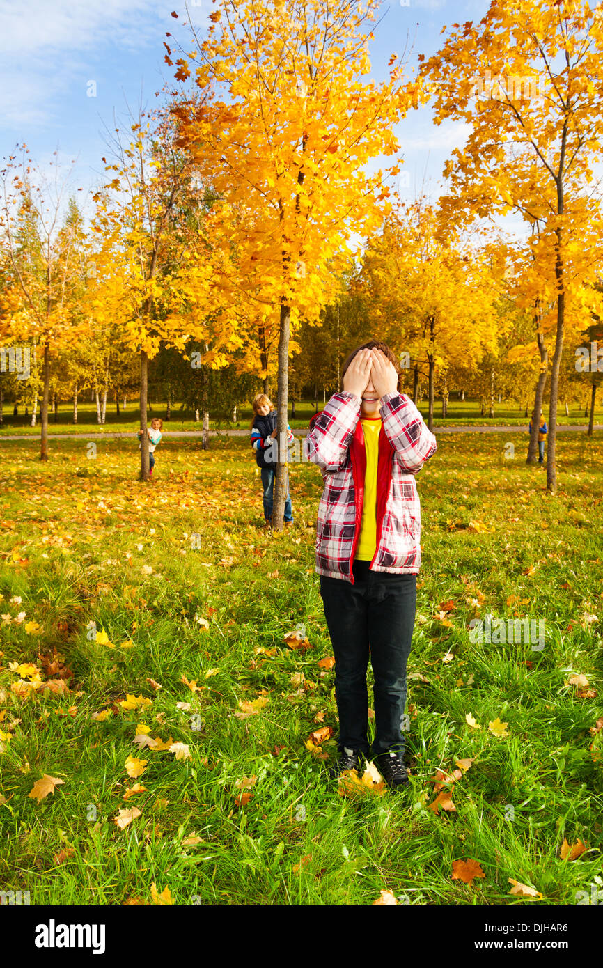 Kinder spielen verstecken und suchen mit jungen zählen Verkleidung Gesicht mit Palmen während andere versteckt sich hinter Herbst männlichen Bäumen Stockfoto