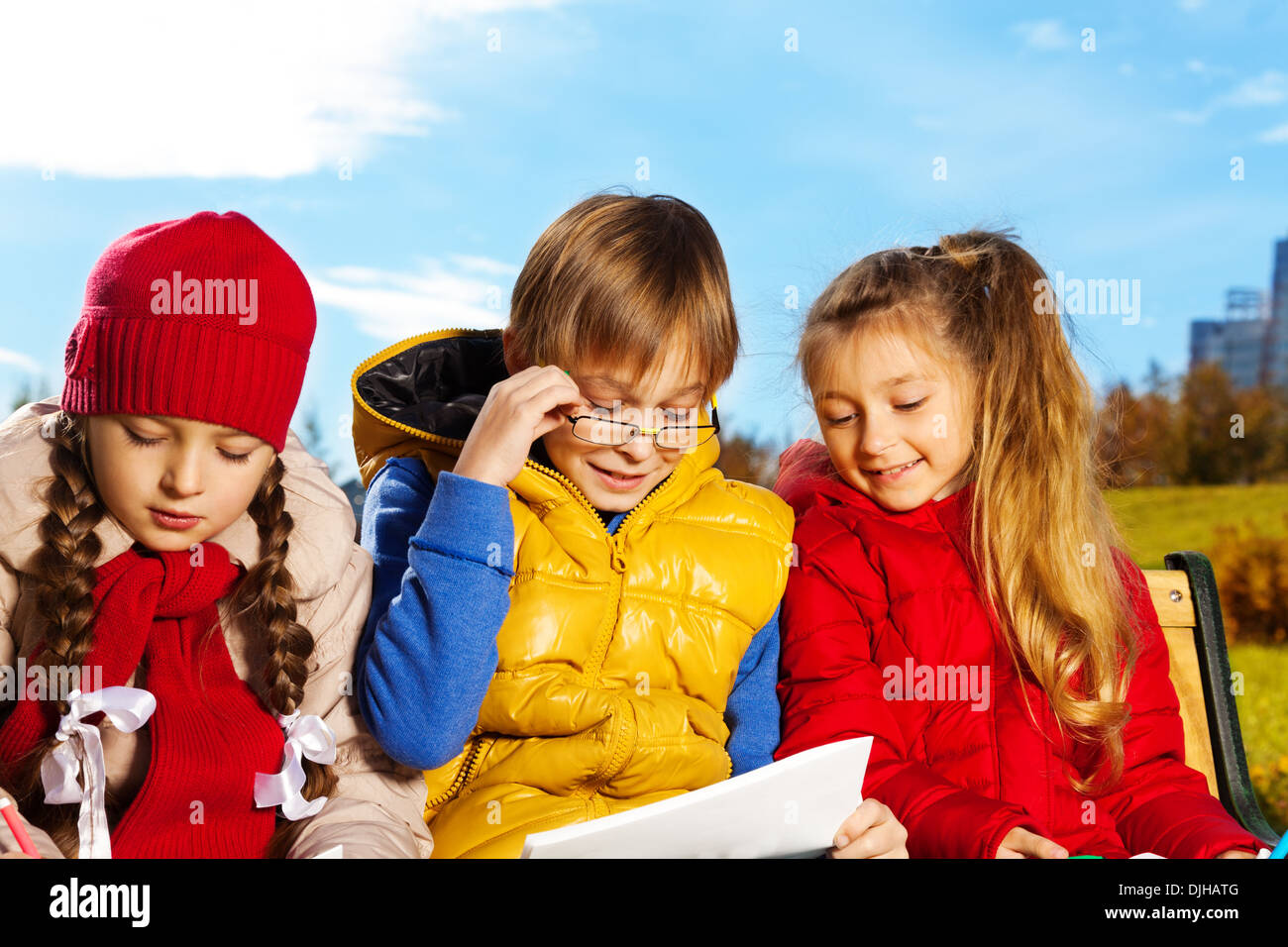 Smart-10 Jahre alter Junge in Brille lesen Sie Papier mit zwei Mädchen-Freunde auf der Bank sitzen Stockfoto