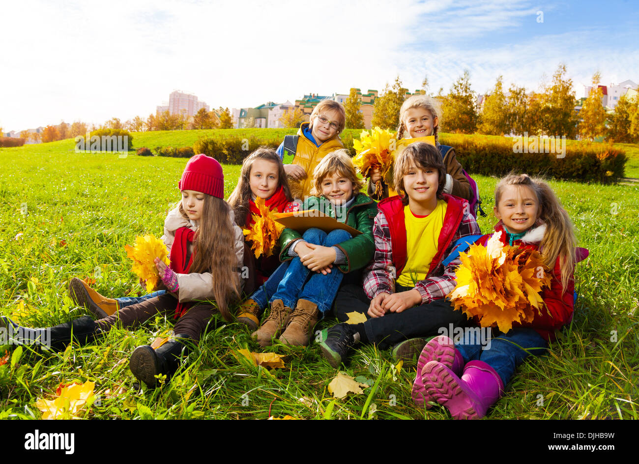 Große Gruppe von Kinder sitzen auf der Wiese im Herbst Kleidung mit Ahorn Blätter, Sträuße und Papiere Stockfoto