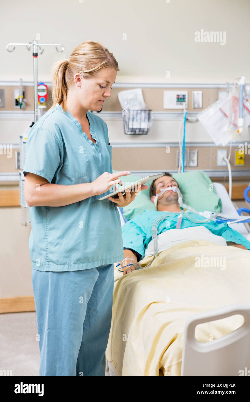Krankenschwester mit Digital-Tablette während der Patient ruht auf Bett Stockfoto