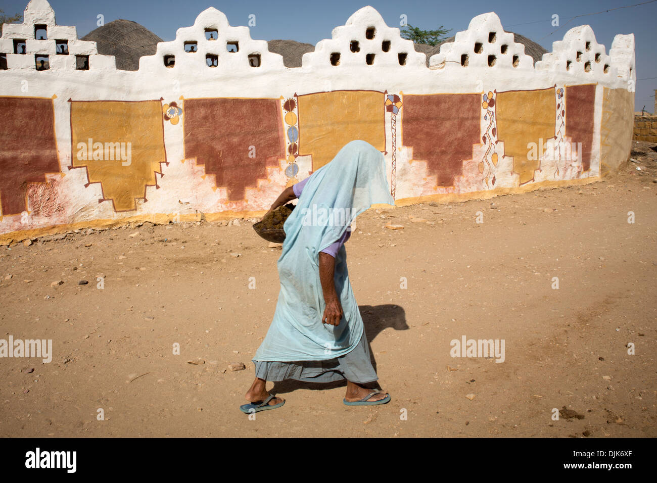 Eine Frau geht entlang der Wand eines Hauses mit Zeichnungen, Farben und Stil dieser nördlichen Region von Rajasthan verziert. Stockfoto