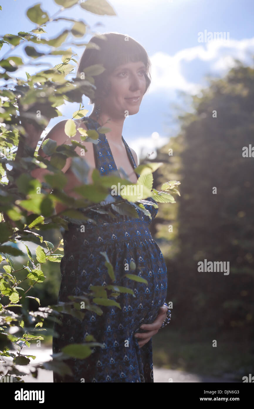 Schwangere Frau in der Nähe von Baum im Hinblick auf Sonnenuntergang Stockfoto