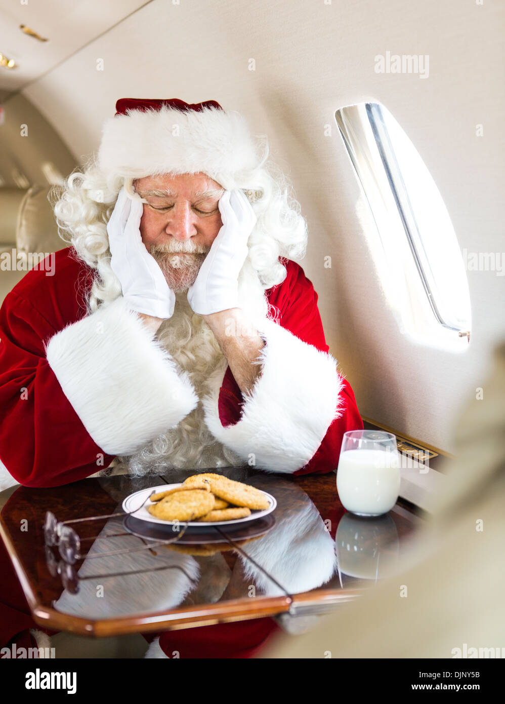 Weihnachtsmann mit Cookies und Milch schlafen im Privatjet Stockfoto
