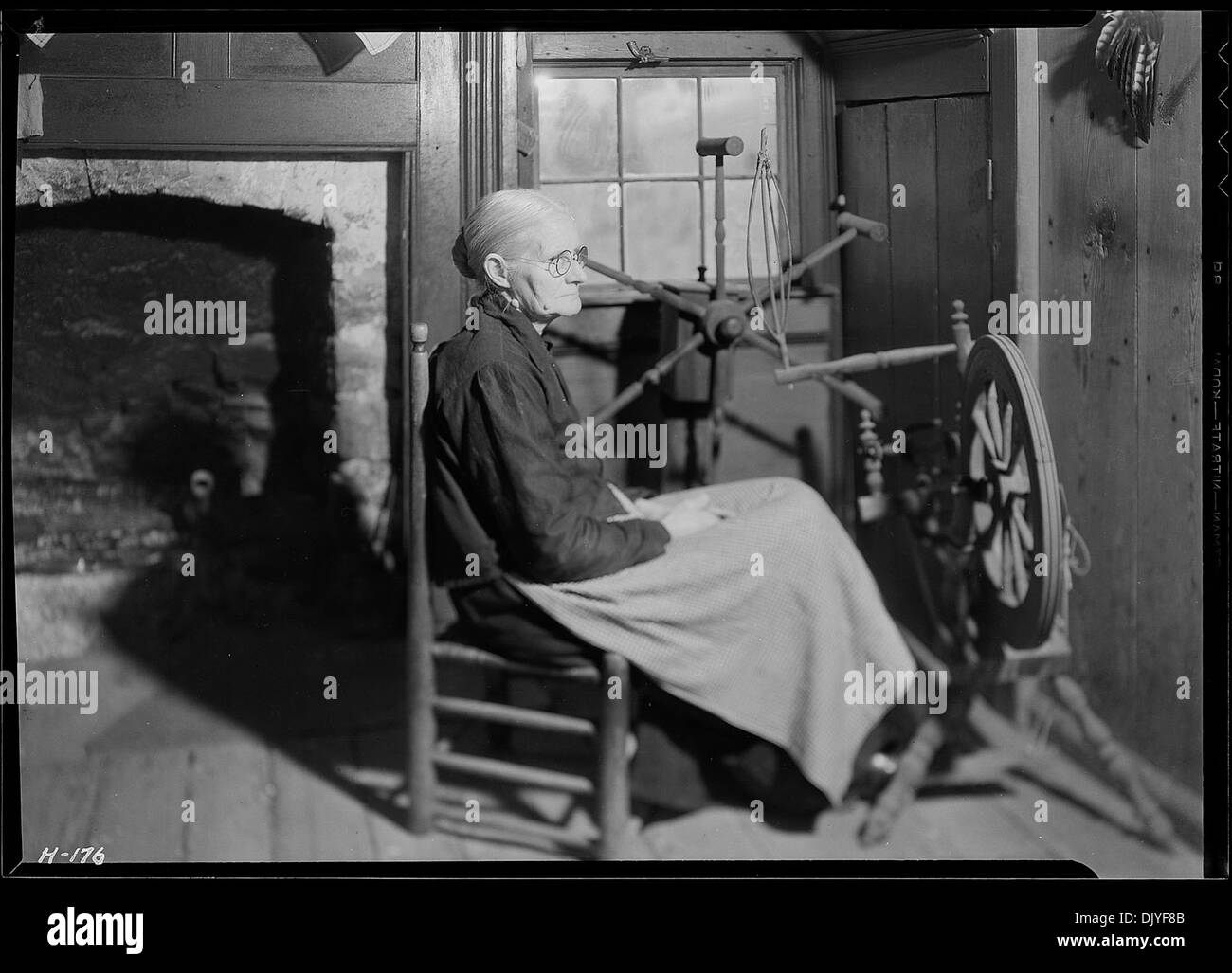 Mrs. Jacob Stooksbury sitzt vor einem drehenden Rad in ihrem Haus in Loyston, Tennessee. Das Bild fängt eine traditionelle Szene des häuslichen Lebens ein, in der Mrs. Stooksbury ein Drehrad für die Stoffproduktion verwendet, eine Praxis, die in der frühen amerikanischen Handwerkskunst verwurzelt ist. Stockfoto