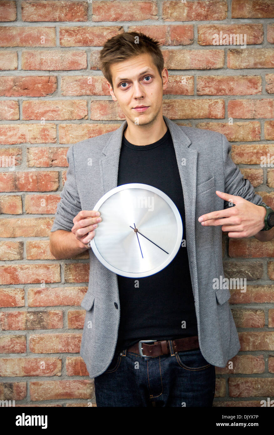 Junger Geschäftsmann hält eine Uhr auf Ziegel Wand Hintergrund. Zeit in Business-Konzept Stockfoto