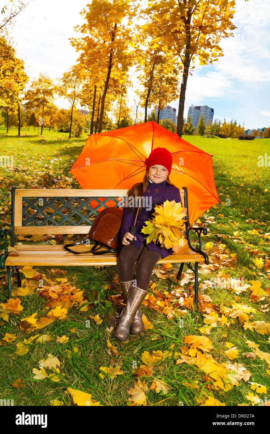 Glückliches kleines Mädchen hält Ahorn Blätter Blumenstrauß sitzt auf der Bank im Herbst Park unter Dach Stockfoto