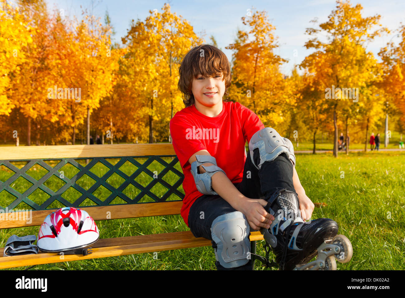 Glücklich 12 Jahre alter Junge sitzt auf der Bank und setzen auf Schlittschuhen im Herbst park Stockfoto