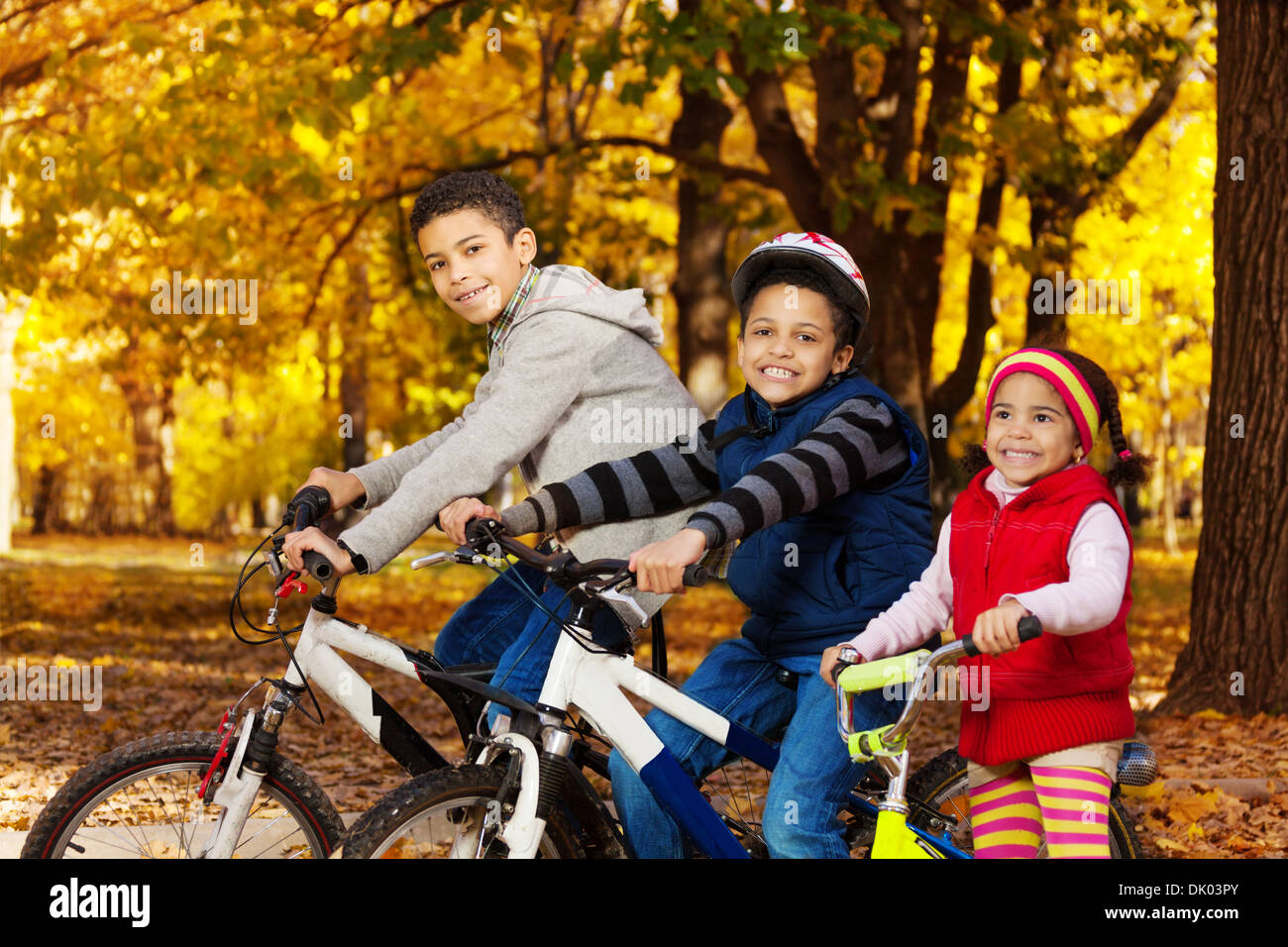 Schließen Portrait von drei schwarzen Jungen und Mädchen, Brüder und Schwester Reiten Fahrräder und Motorroller im Herbst Oktober park mit Maple Leaves Stockfoto