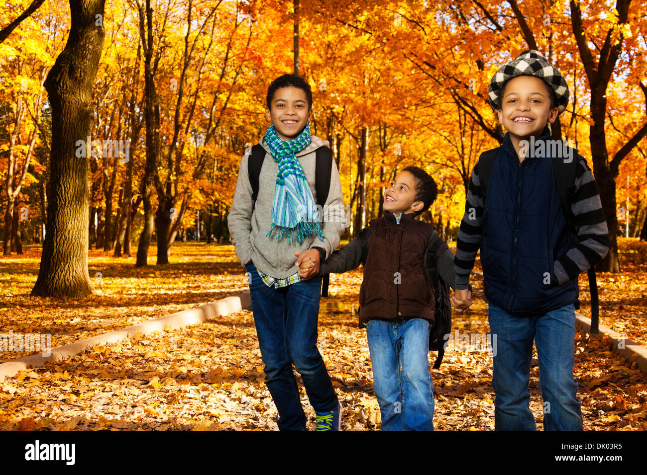 Drei schwarzen Jungen, gerne Brüder 5-10 Jahre zusammen gehen Hand in Hand im Park tragen Rucksäcke und Herbst Kleidung in Maple Park Stockfoto