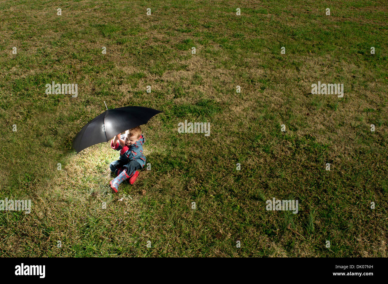 Eine 3-jährige Junge spielt mit einem schwarzen Schirm heraus in einem Feld in Pittsboro, NC. Er trägt einen Regenmantel und Stiefel Stockfoto