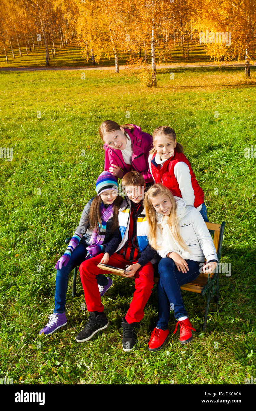 Portrait von Fünf glückliche Kinder, Jungen und Mädchen früh jugendlich Schule alter Suchen in Kameras draußen sitzen mit Boy holding Tablet-PC Stockfoto
