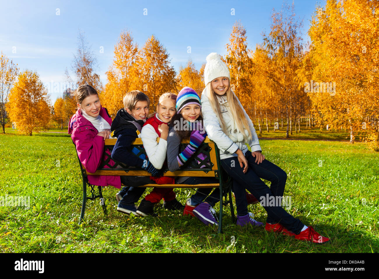 Fünf schulpflichtigen Alter jugendlich Kinder sitzen auf der Bank im herbstlichen Park und drehen mit Lächeln und glückliche Gesichter zurück Stockfoto