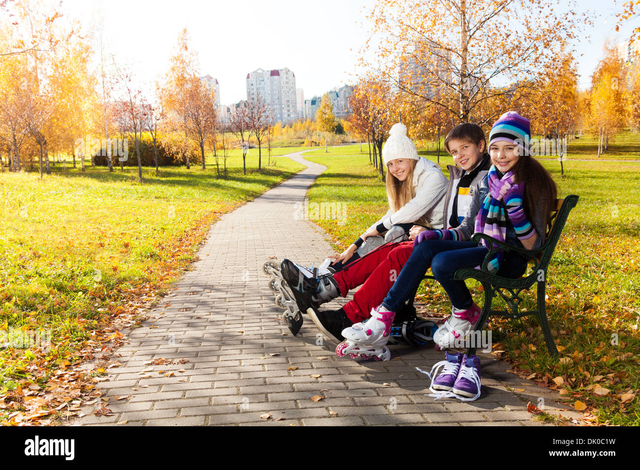 Zwei Mädchen und ein Junge auf Rollerblades sitzen auf der Bank im park Stockfoto